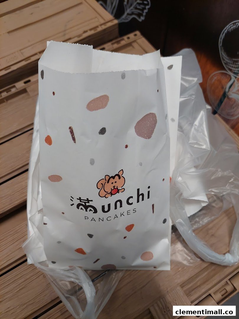 A white paper bag from Munchi Pancakes featuring a cute squirrel logo and colorful speckles.