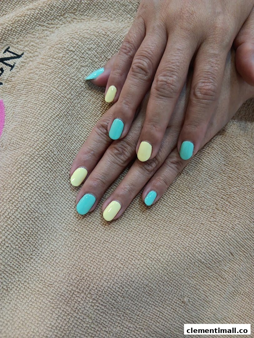 A close-up of hands with freshly painted nails in alternating pastel yellow and turquoise colors.