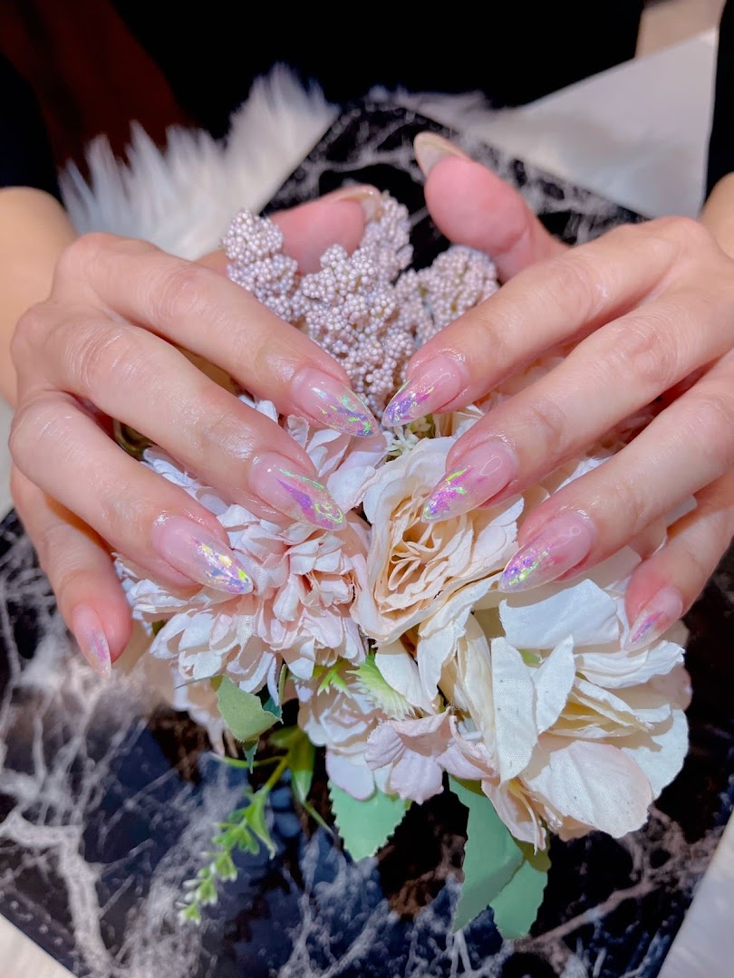 Close-up of hands showcasing elegant, long nails with iridescent glitter accents, holding a bouquet of flowers.