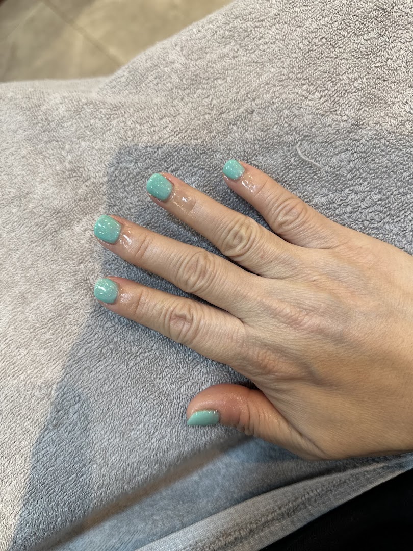 A hand with freshly painted light green nails resting on a grey towel, showcasing a manicure.