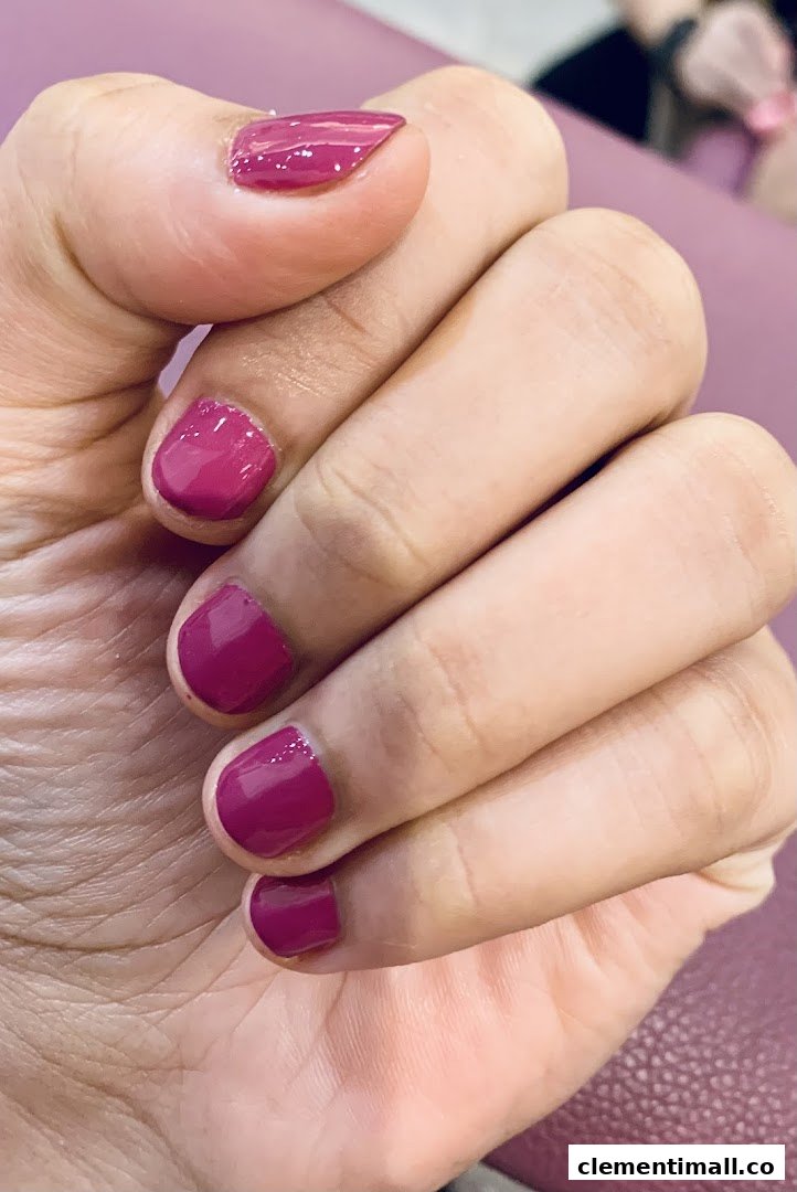 A close-up of a hand showcasing freshly painted magenta nails, highlighting a nail service.