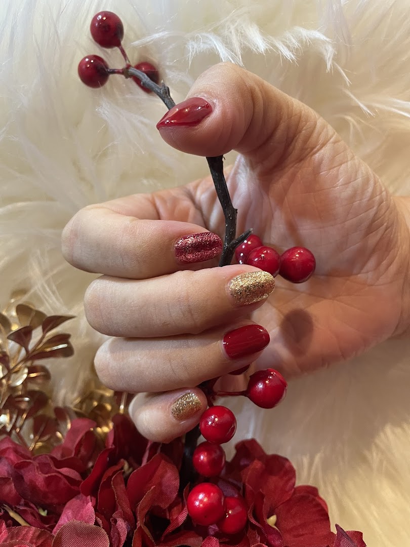 A hand with festive red and gold glitter manicured nails holding a decorative berry branch.