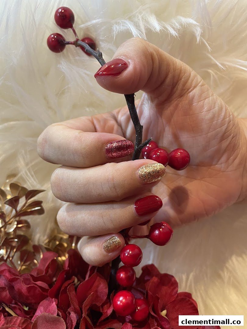 A hand with festive red and gold glitter manicured nails holding a decorative berry branch.