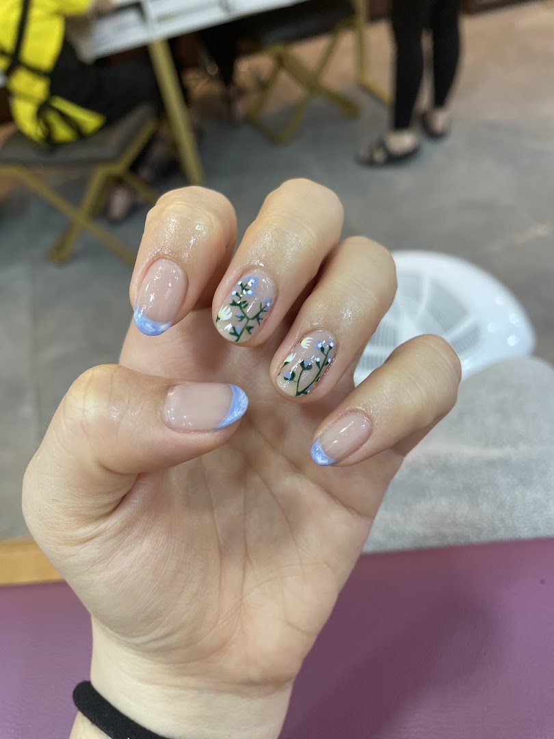 A hand showcasing a fresh manicure with light blue French tips and delicate floral nail art.
