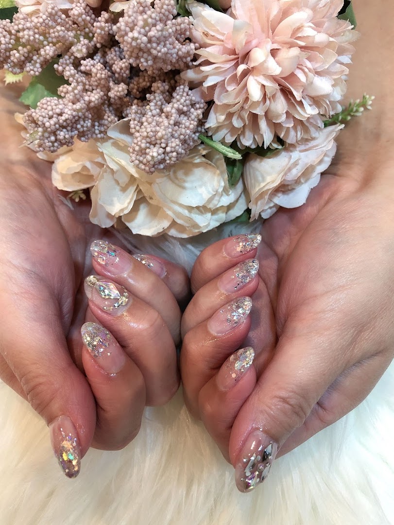 Close-up of hands showcasing sparkling glitter and gem nail art, holding delicate pink and cream flowers.