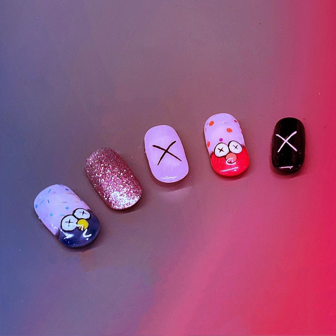 Close-up of five artificial nails showcasing diverse and creative nail art designs, including glitter and cartoon characters.