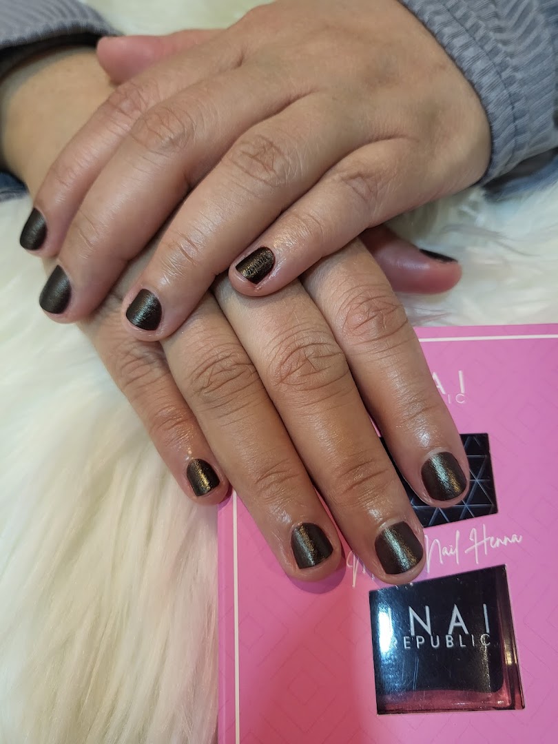 A close-up of hands with dark, shimmery nail polish, resting on a white furry surface next to a pink product box.