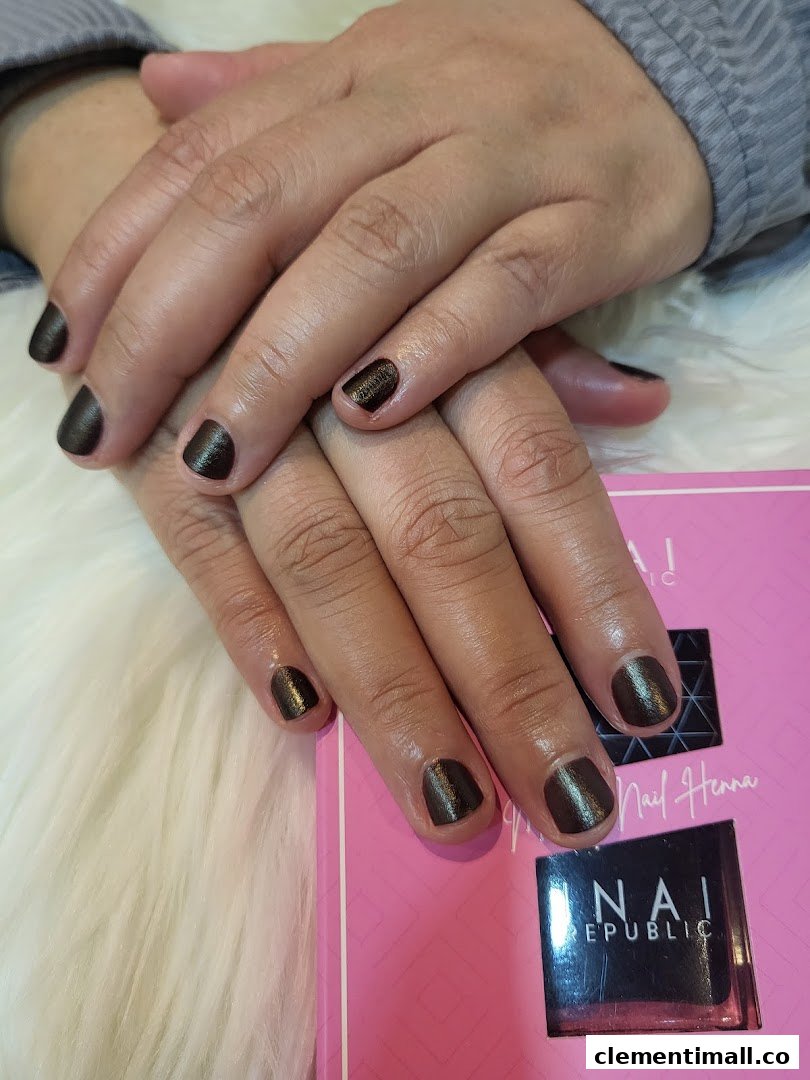 A close-up of hands with dark, shimmery nail polish, resting on a white furry surface next to a pink product box.