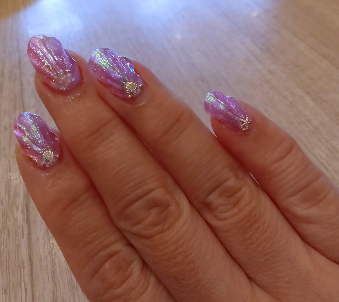 Close-up of a hand showcasing iridescent purple seashell-themed nail art with delicate charms.