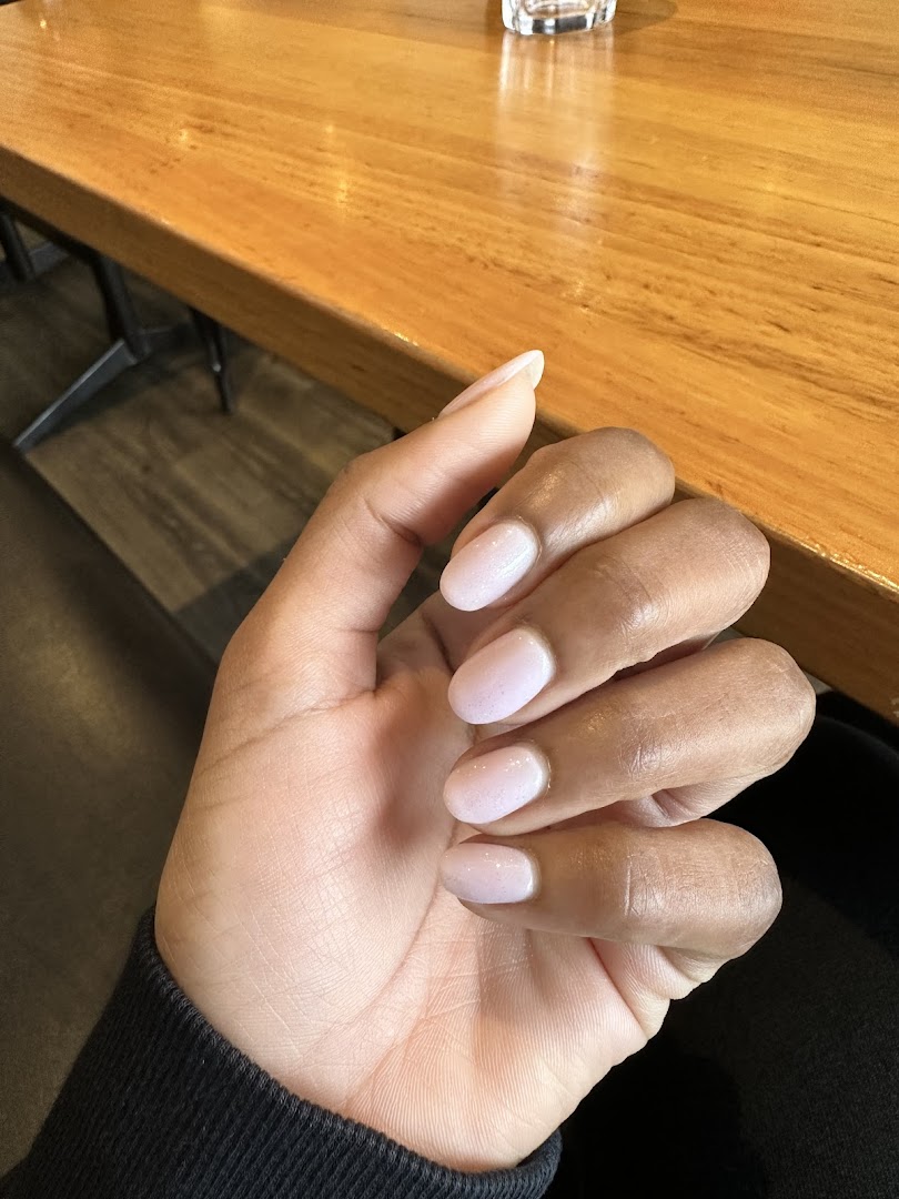 A hand showcasing light pink, glittery manicured nails resting on a wooden table.