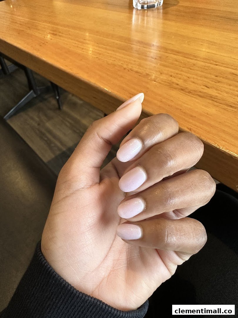 A hand showcasing light pink, glittery manicured nails resting on a wooden table.
