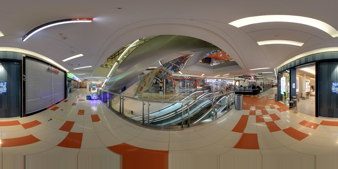 A panoramic view of a modern shopping mall interior with various retail shops and escalators.