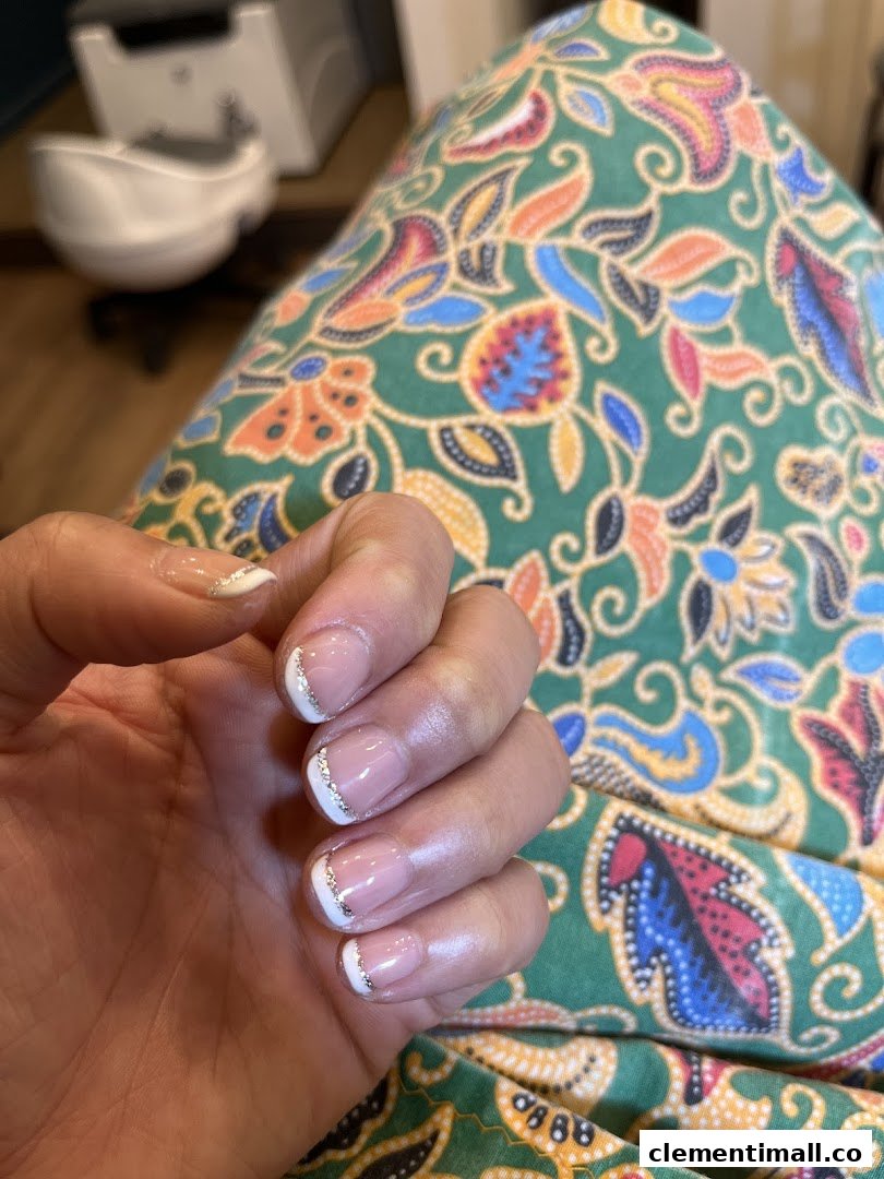 A close-up of a hand showcasing a fresh French manicure with elegant silver glitter accents.