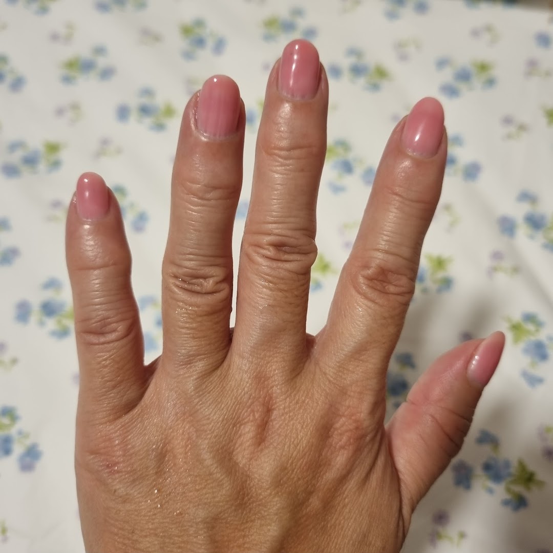 A hand showcasing freshly manicured nails with a soft pink polish against a floral background.