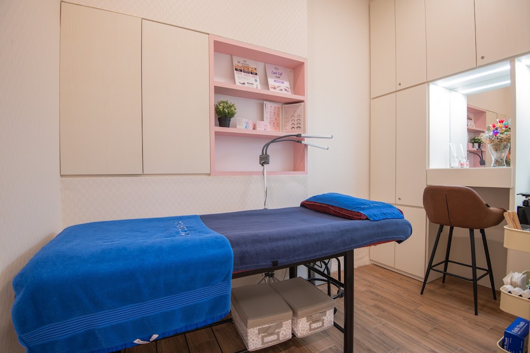 A clean, modern beauty treatment room with a treatment bed, product shelves, and vanity area.