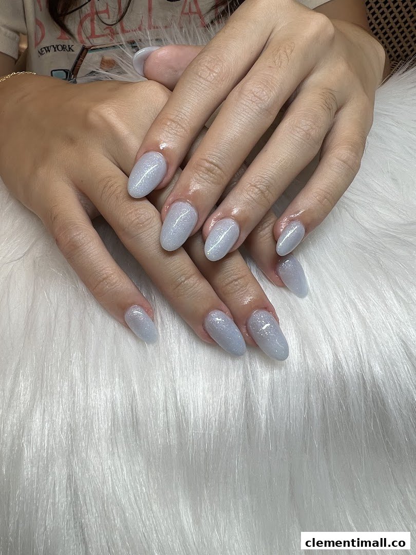 Close-up of hands showcasing light blue glitter nail polish on a white furry surface.