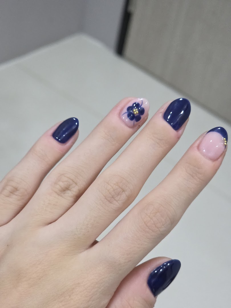 A hand showcasing elegant dark blue nail polish with a delicate floral accent on one nail.