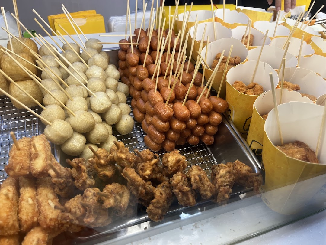 A close-up view of various fried snacks, including fish balls, sausages on skewers, and fried chicken pieces.