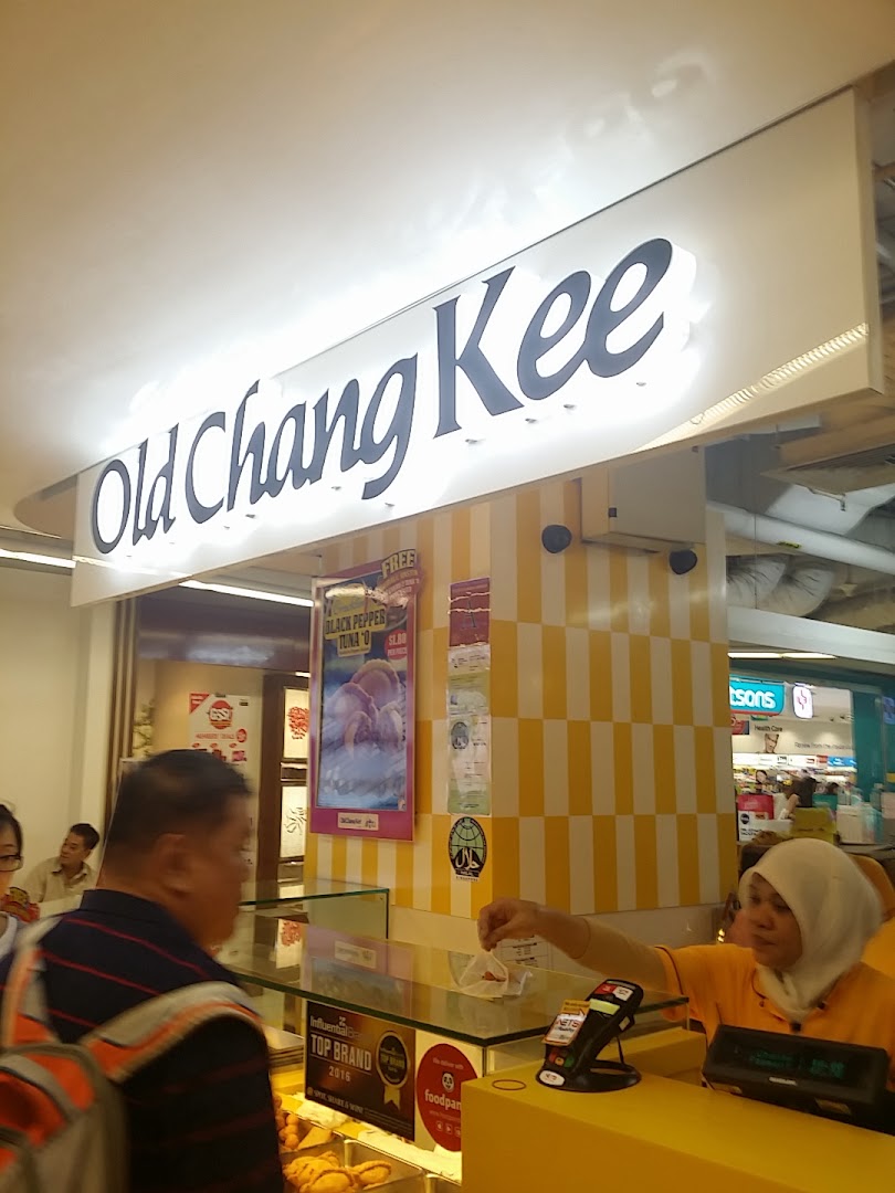 A bustling Old Chang Kee counter with a staff member serving a customer under the shop's illuminated sign.