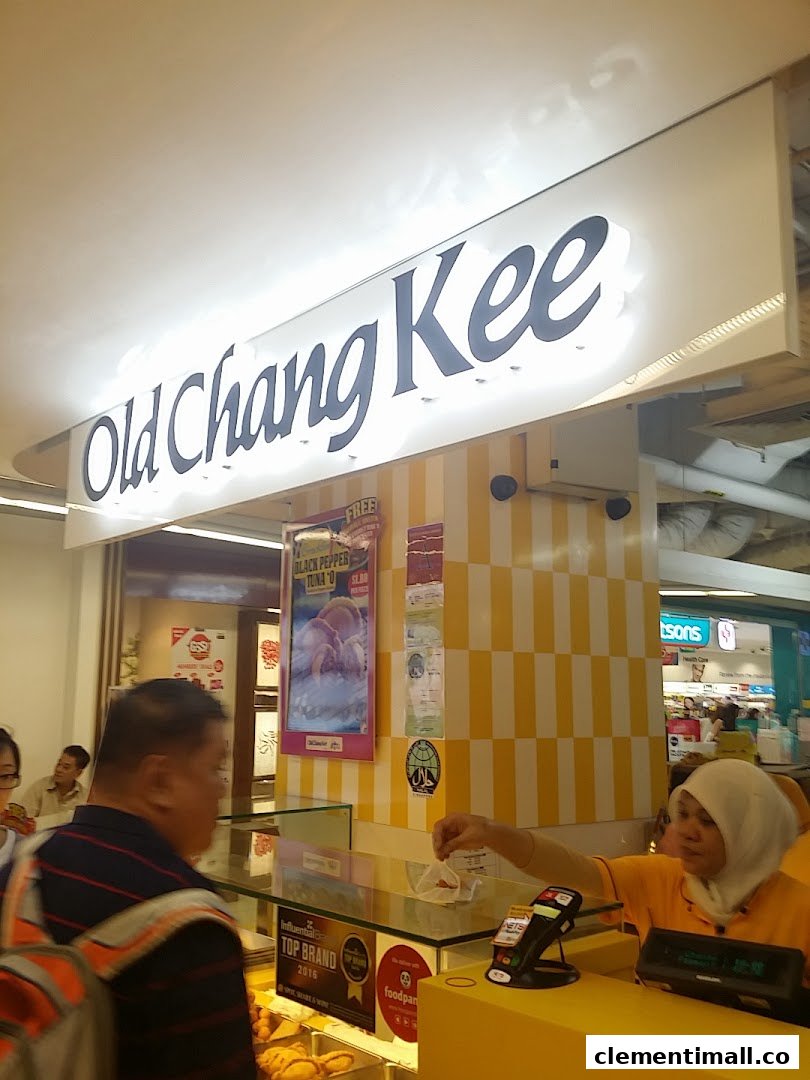 A bustling Old Chang Kee counter with a staff member serving a customer under the shop's illuminated sign.