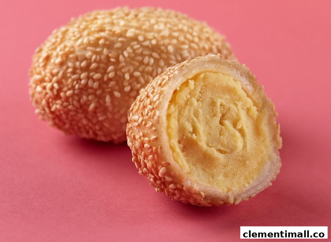 A golden sesame ball, one cut open to reveal its sweet, yellow filling, on a pink background.