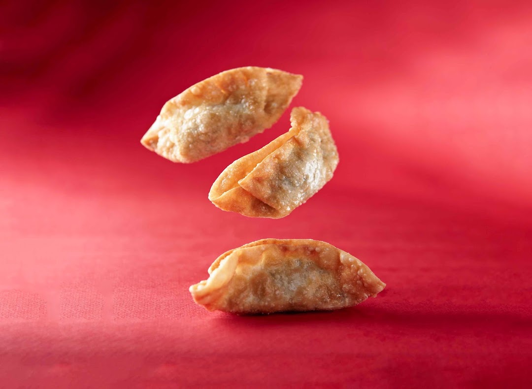 Three golden-fried dumplings float against a vibrant red background, showcasing a delicious snack.