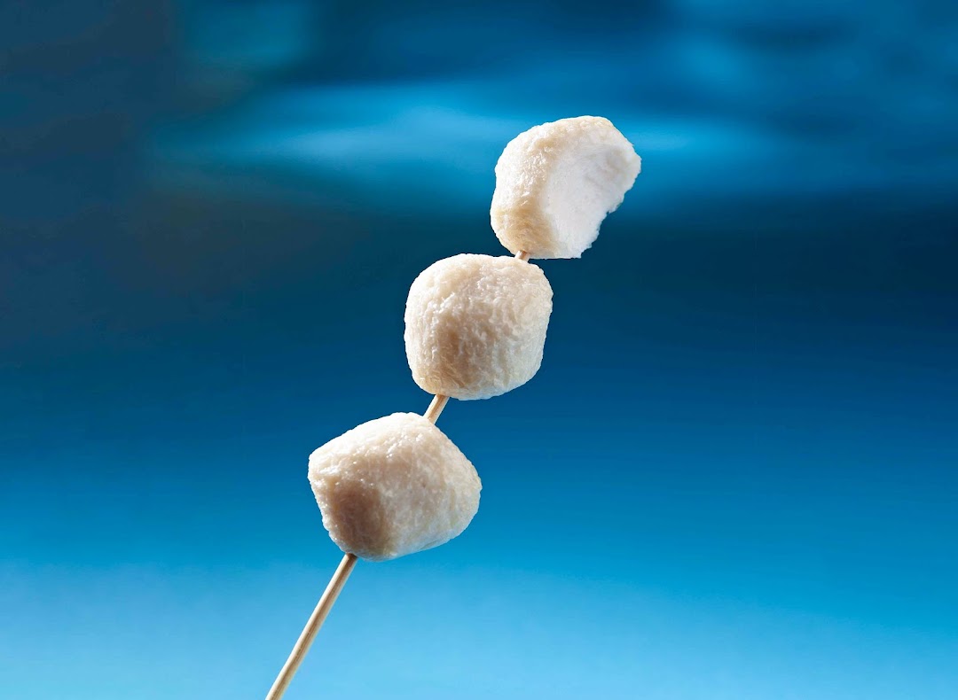 Three white fishballs on a wooden skewer against a vibrant blue background.