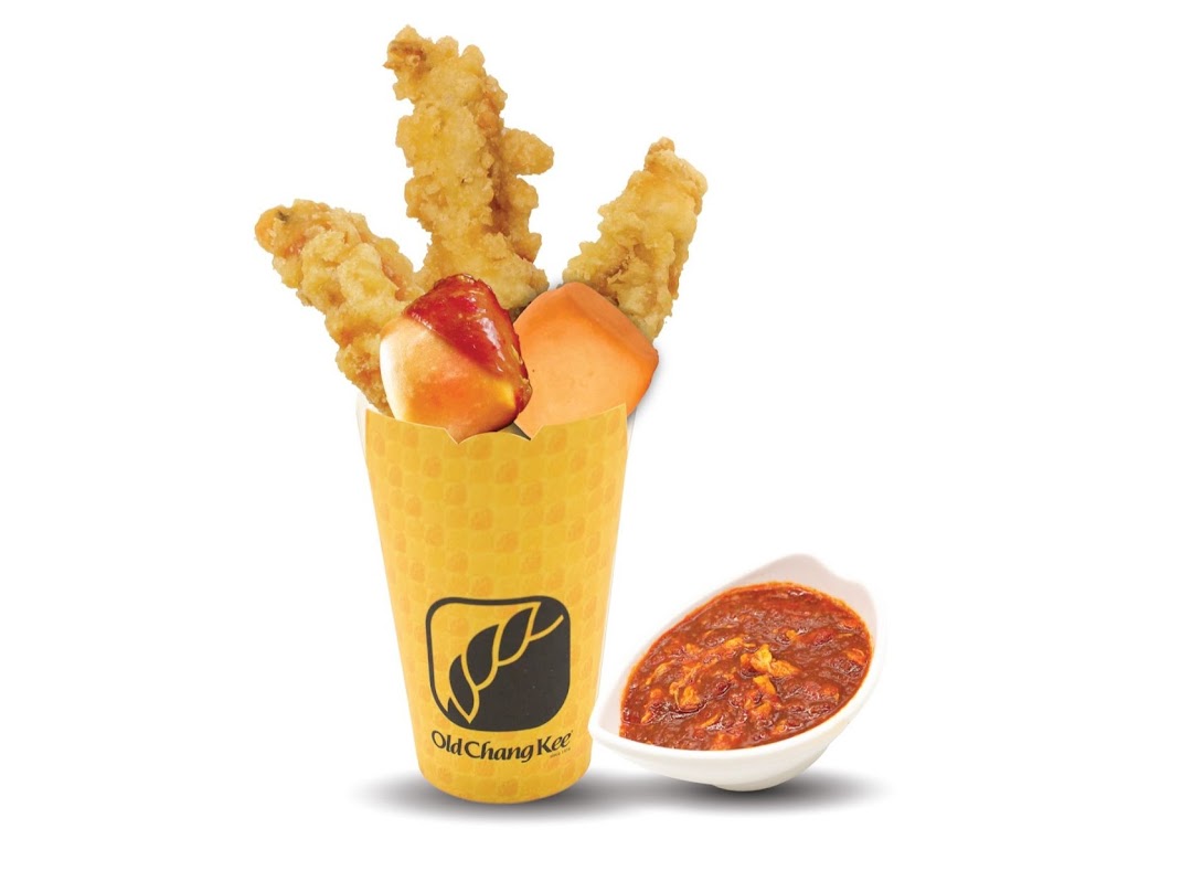 A yellow cup filled with fried snacks, including chicken and a fishball, with a side of chili sauce.