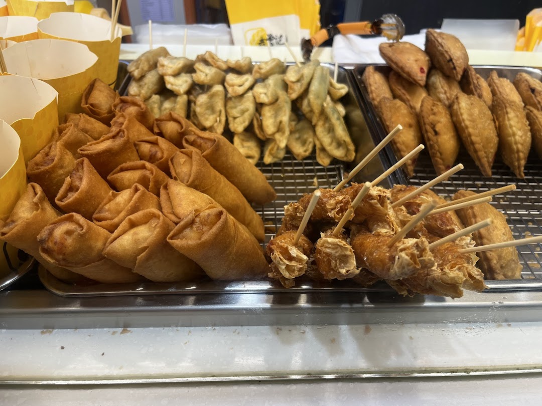 A vibrant display of golden-fried snacks including spring rolls, curry puffs, and other fried items.