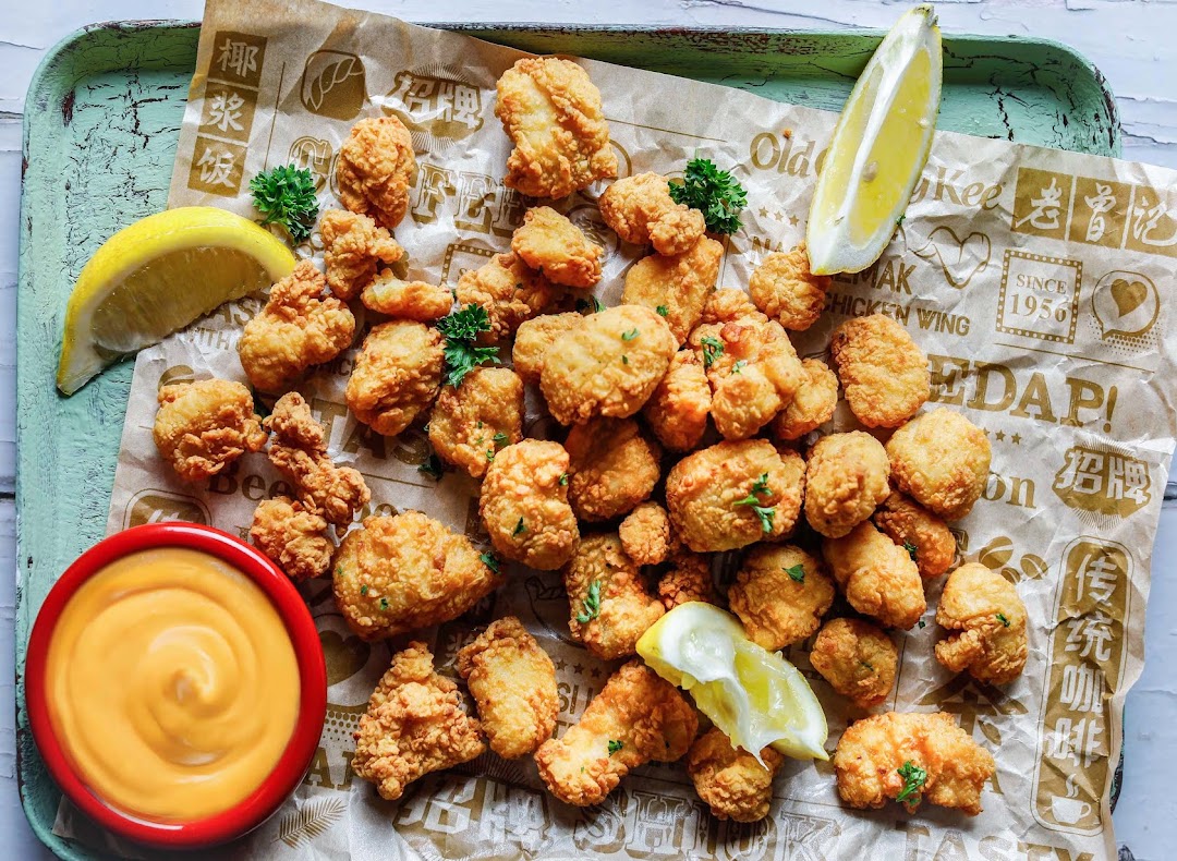 Golden fried bites, possibly chicken or prawns, with dipping sauce and lemon on branded paper.