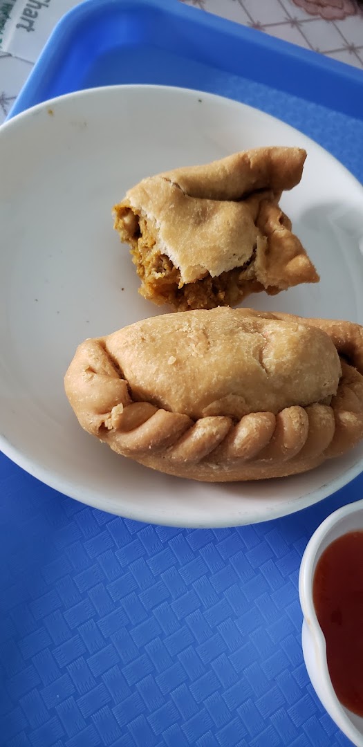 Two golden-brown curry puffs on a white plate, one revealing its savory filling, with a side of chili sauce.