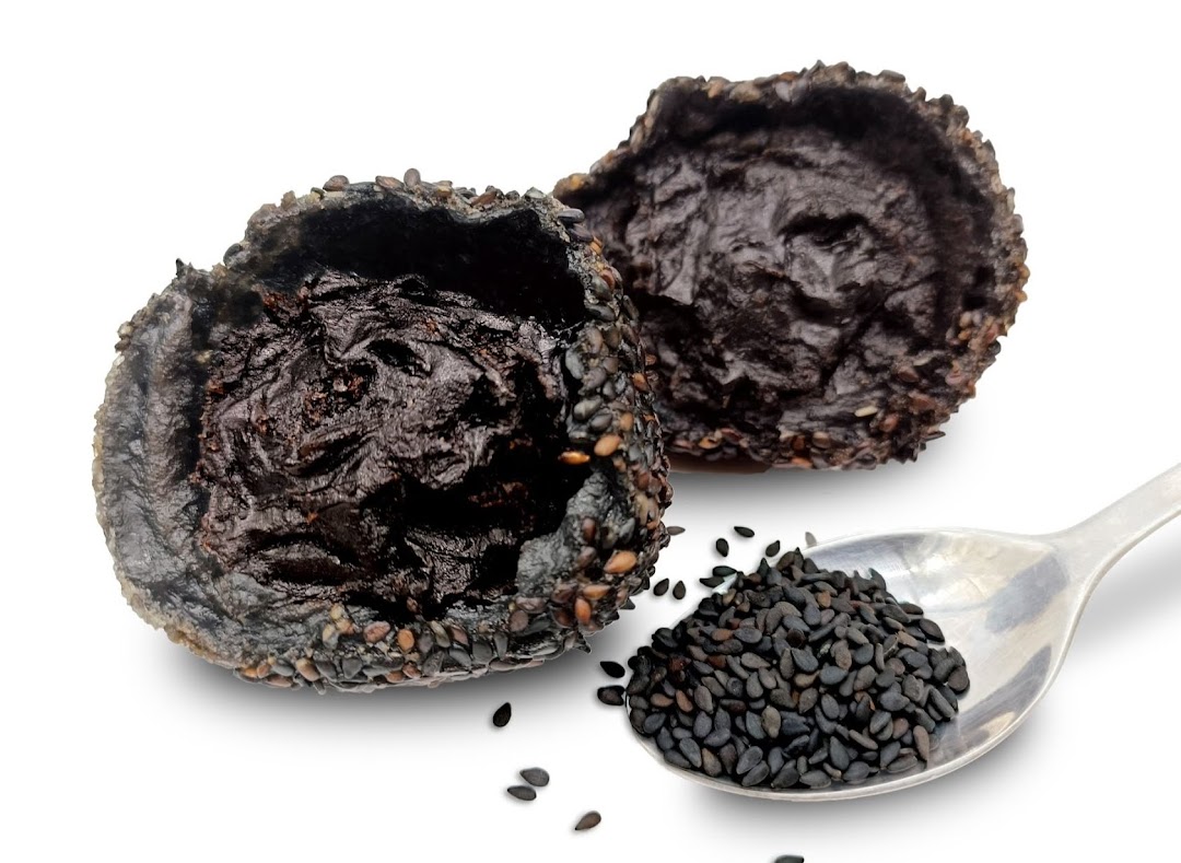 Two dark, sesame-coated pastries with a spoon of black sesame seeds on a white background.