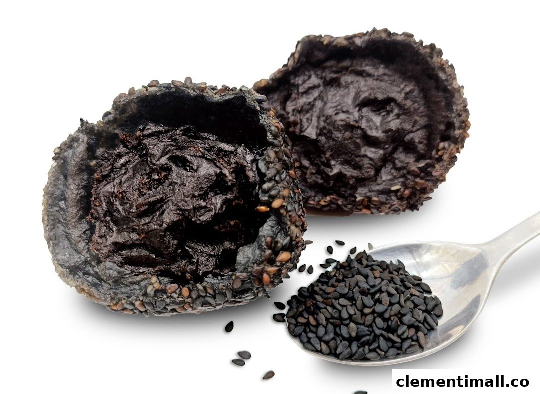 Two dark, sesame-coated pastries with a spoon of black sesame seeds on a white background.