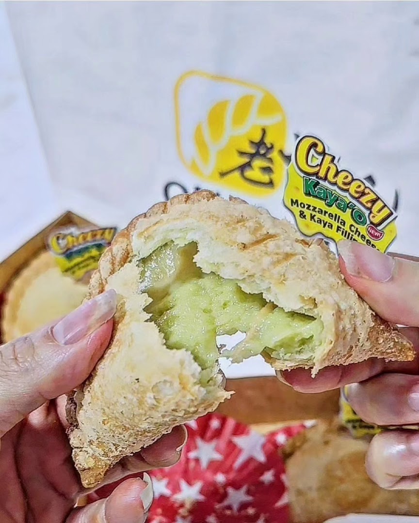 A hand holds a Cheezy Kaya'O puff from Old Chang Kee, revealing its green kaya and mozzarella filling.