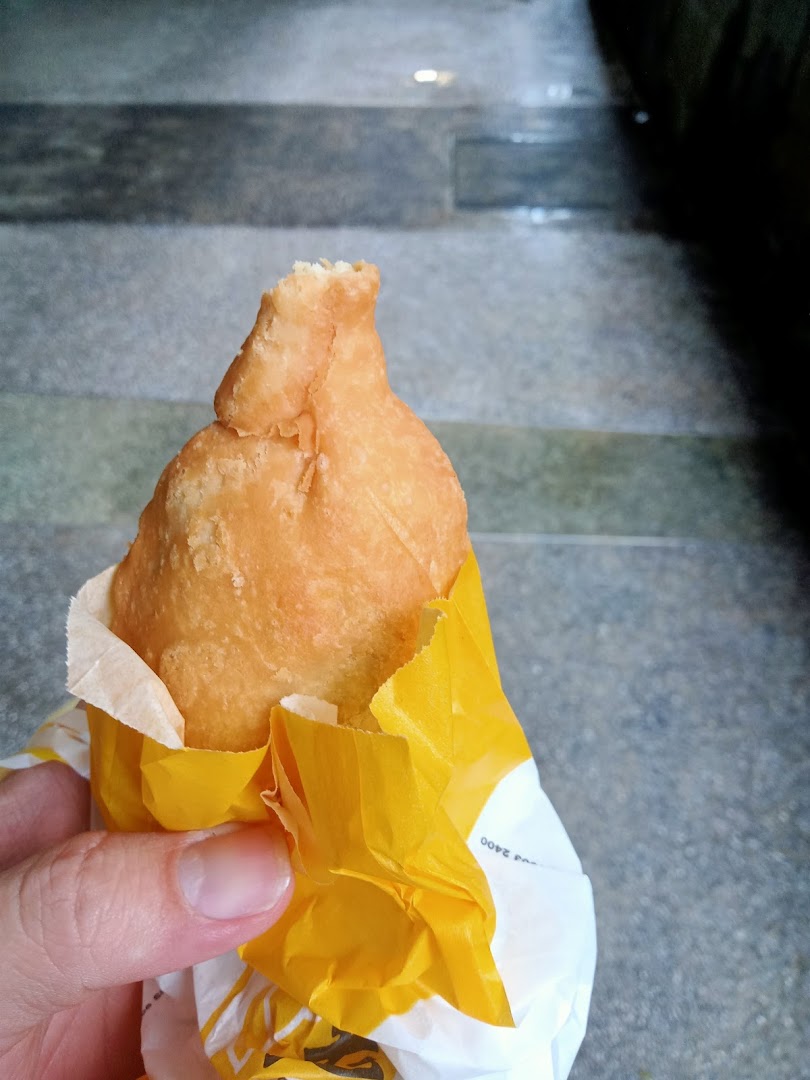A hand holds a golden-fried puff from Old Chang Kee, wrapped in yellow paper.