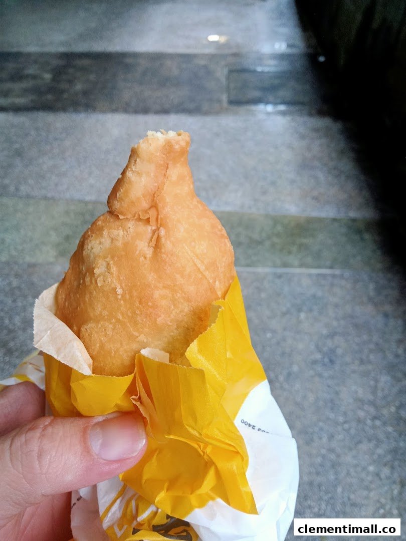 A hand holds a golden-fried puff from Old Chang Kee, wrapped in yellow paper.