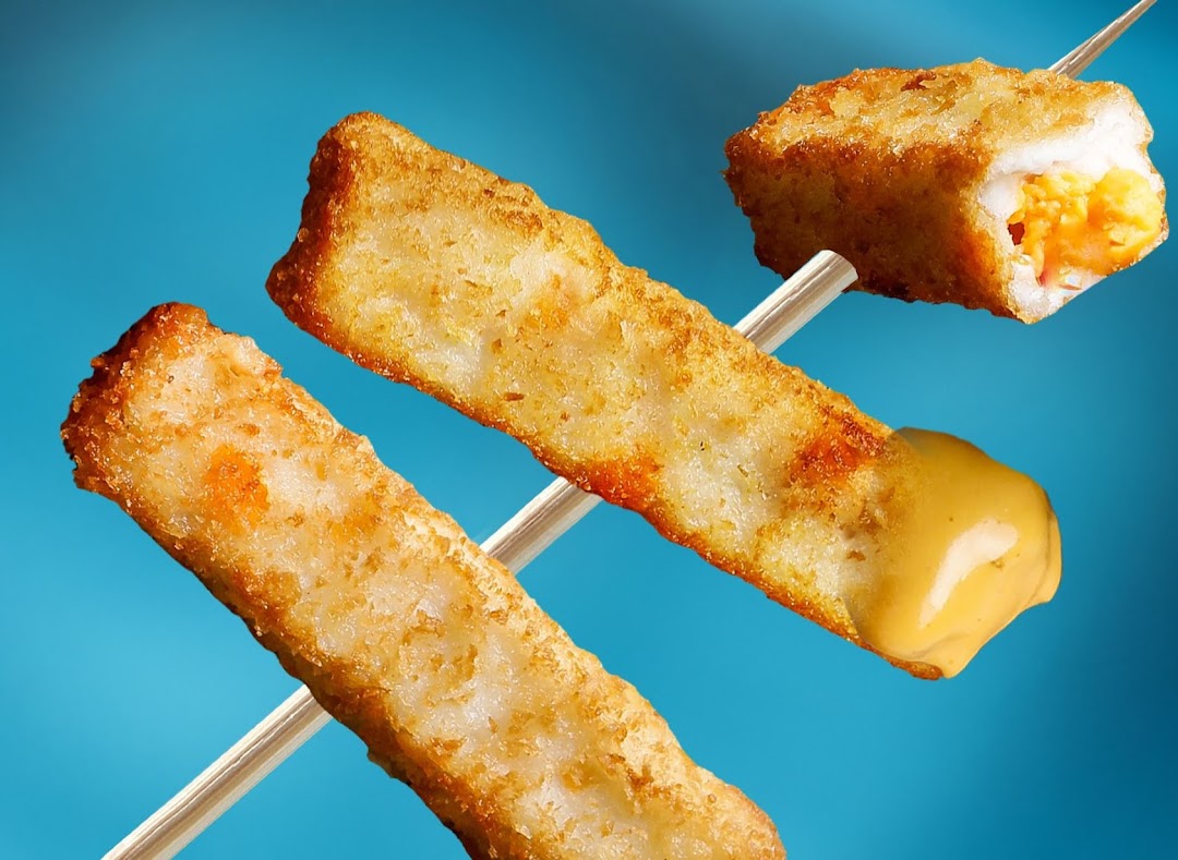 Close-up of golden-fried snacks on skewers, one with a creamy sauce and another revealing a savory filling.