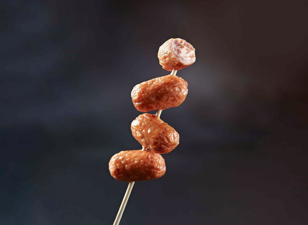 A close-up of golden-brown fried fishballs on a skewer, with one bitten to reveal its texture.