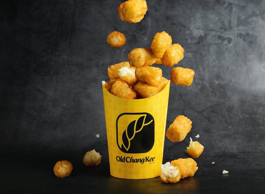 A yellow Old Chang Kee cup filled with golden, crispy tater tots against a dark background.