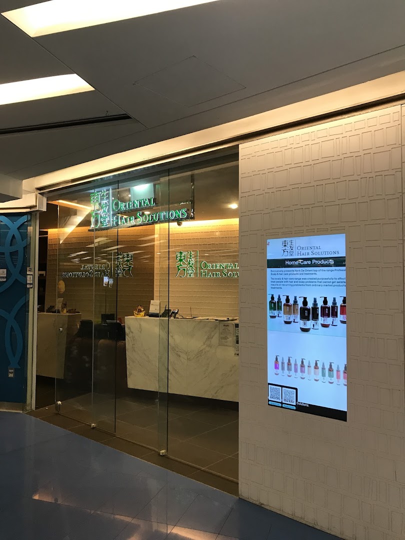 The illuminated glass entrance of Oriental Hair Solutions, featuring a digital display showcasing home-care products.