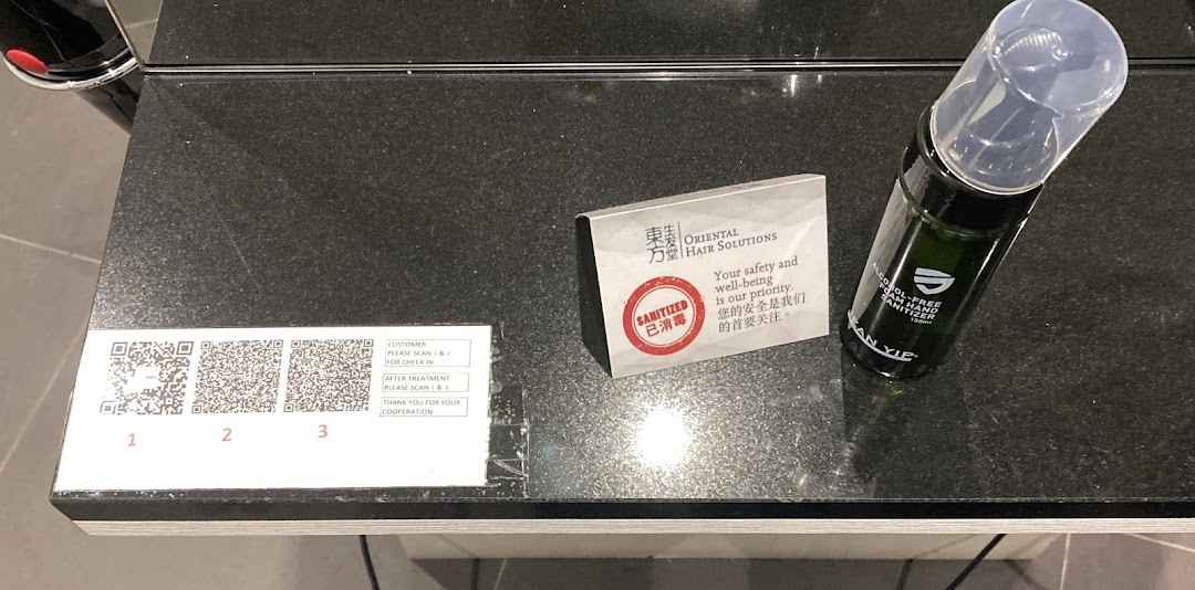A counter with QR codes for check-in/out, a 'sanitized' sign, and hand sanitizer at Oriental Hair Solutions.