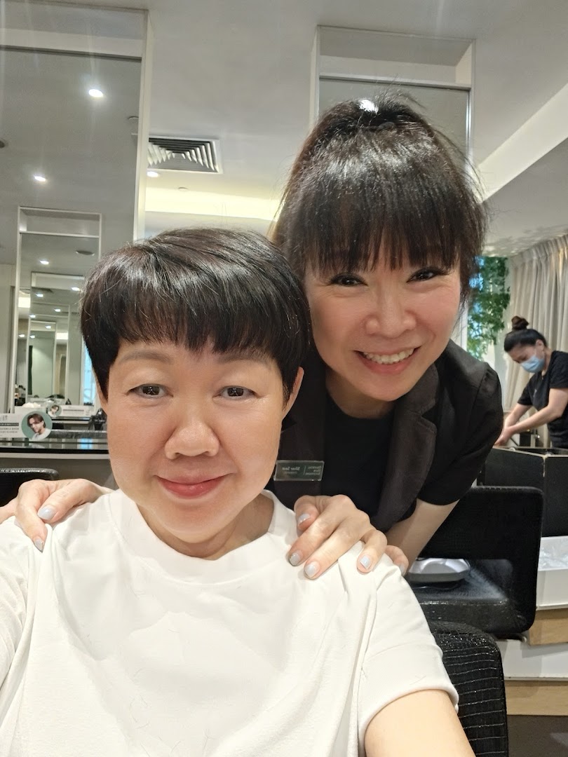 Two smiling women, a customer and a stylist, in a modern hair salon setting.