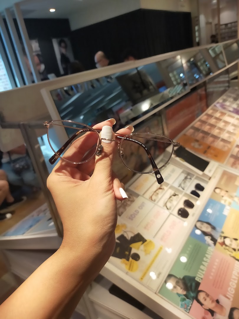 A hand holds a pair of stylish eyeglasses inside the OWNDAYS optical shop.