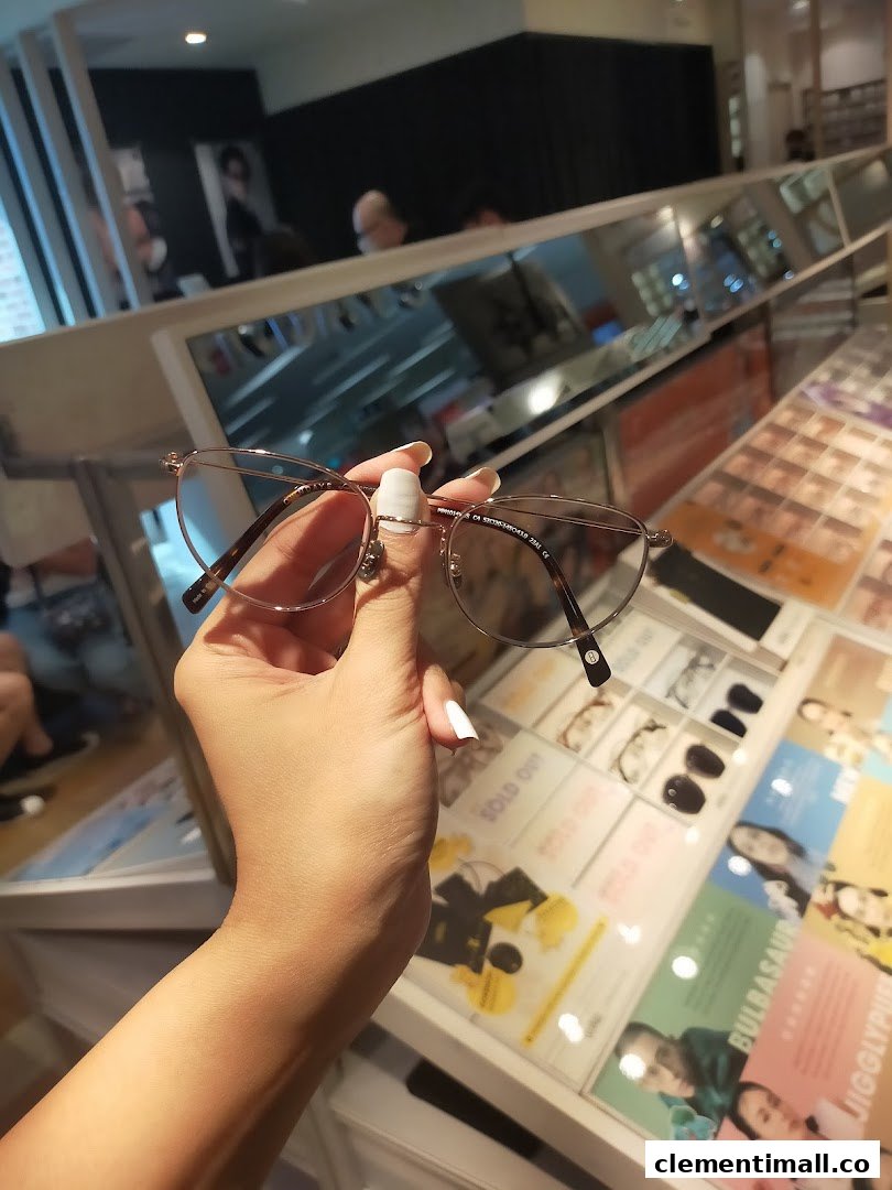 A hand holds a pair of stylish eyeglasses inside the OWNDAYS optical shop.