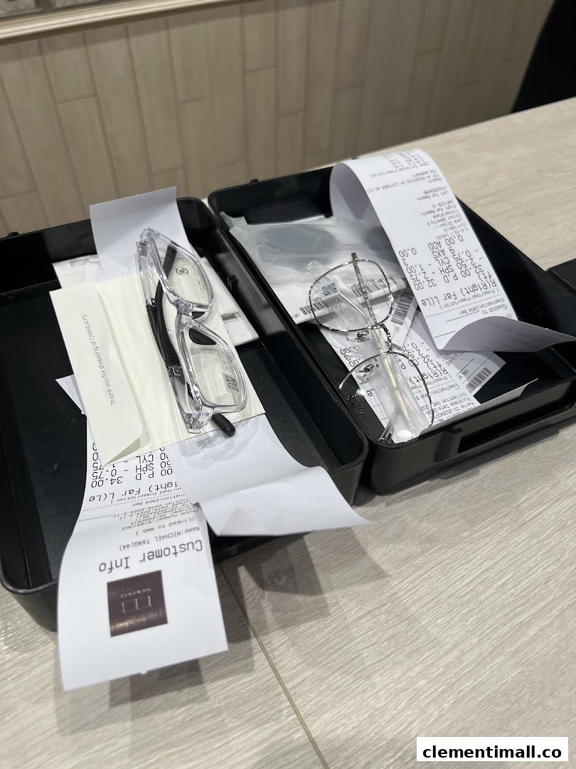 Two pairs of eyeglasses with receipts and packaging in a black case on a wooden surface.