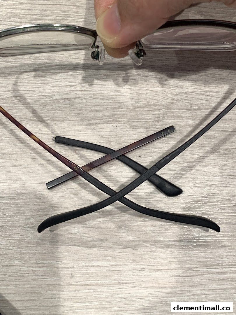 A hand holds eyeglasses, with detached temples lying on a wooden surface, suggesting repair or assembly.