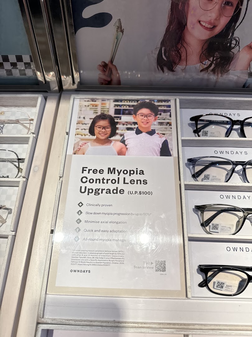 A display at OWNDAYS featuring a promotional sign for free myopia control lens upgrade and various eyewear frames.