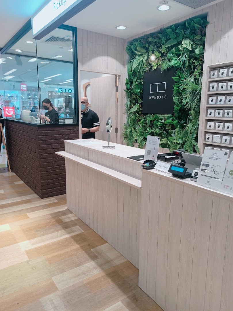 Interior view of OWNDAYS Clementi Mall, featuring the service counter, staff, and a green wall.