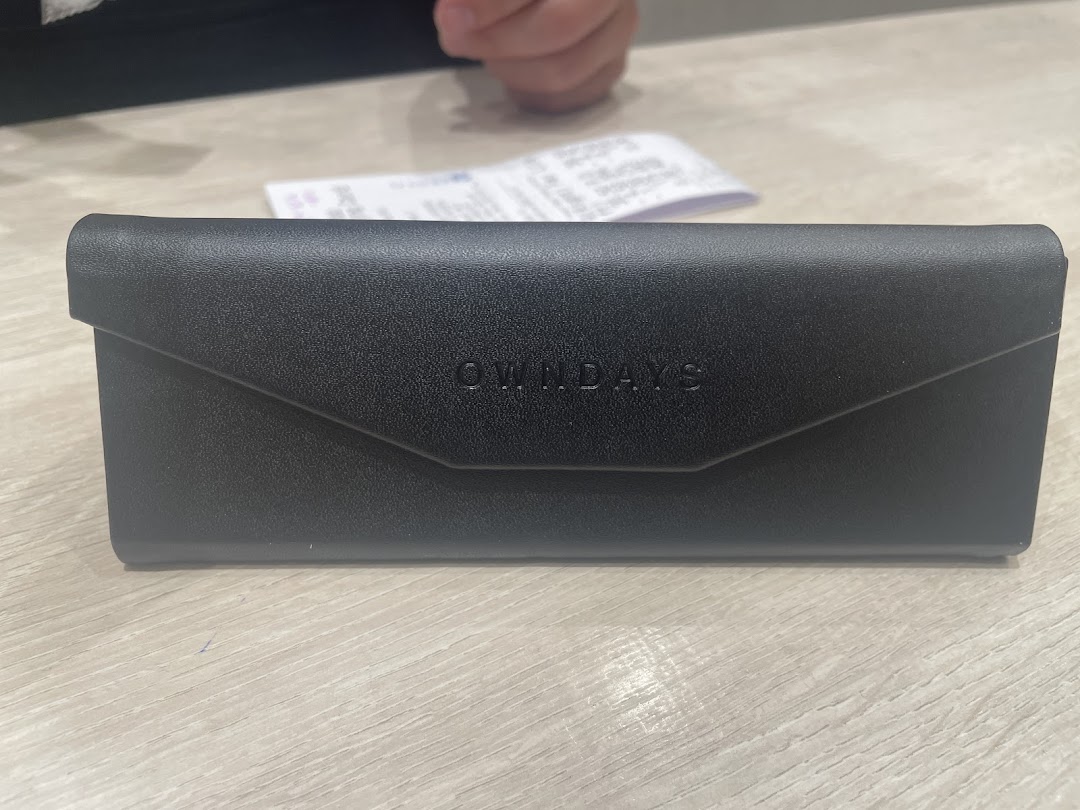 A sleek black OWNDAYS glasses case with embossed logo, resting on a light-colored table.