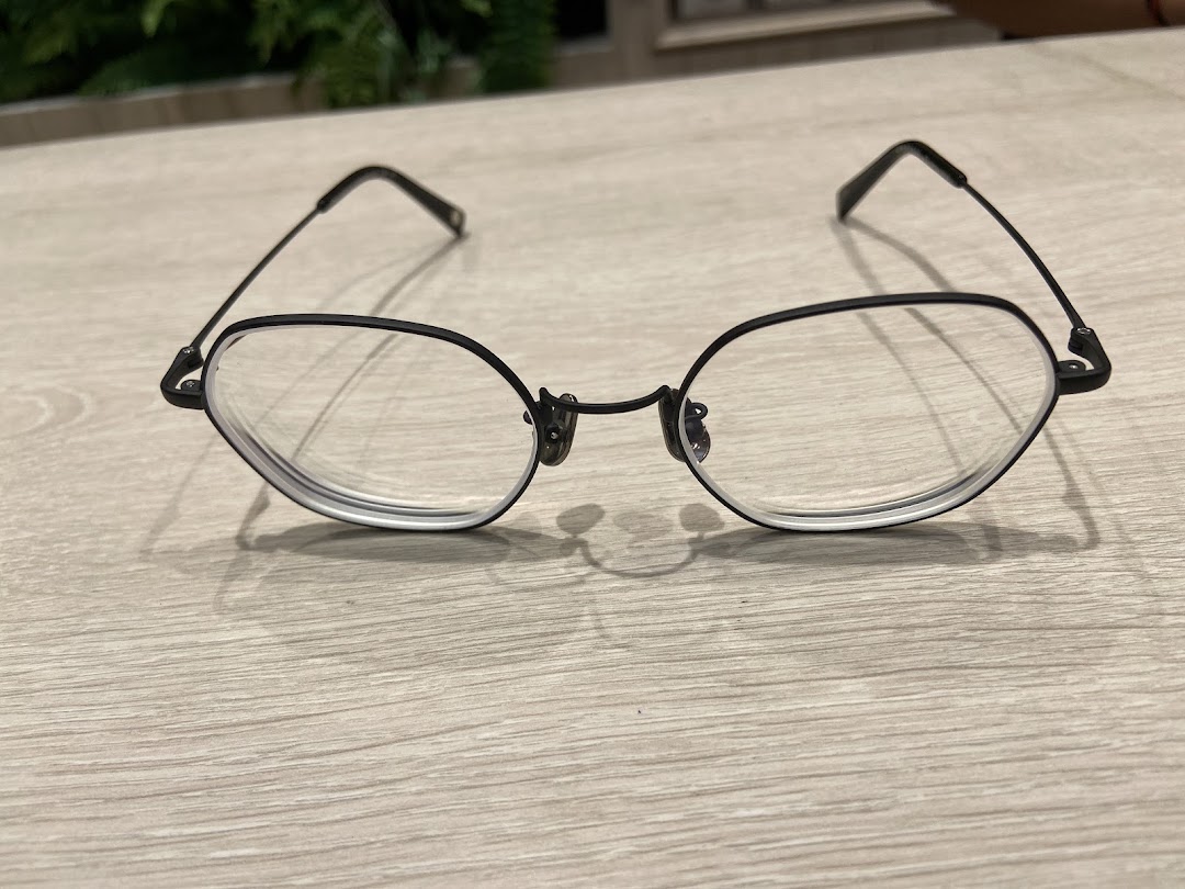 A stylish pair of black-framed eyeglasses rests on a light wooden surface.